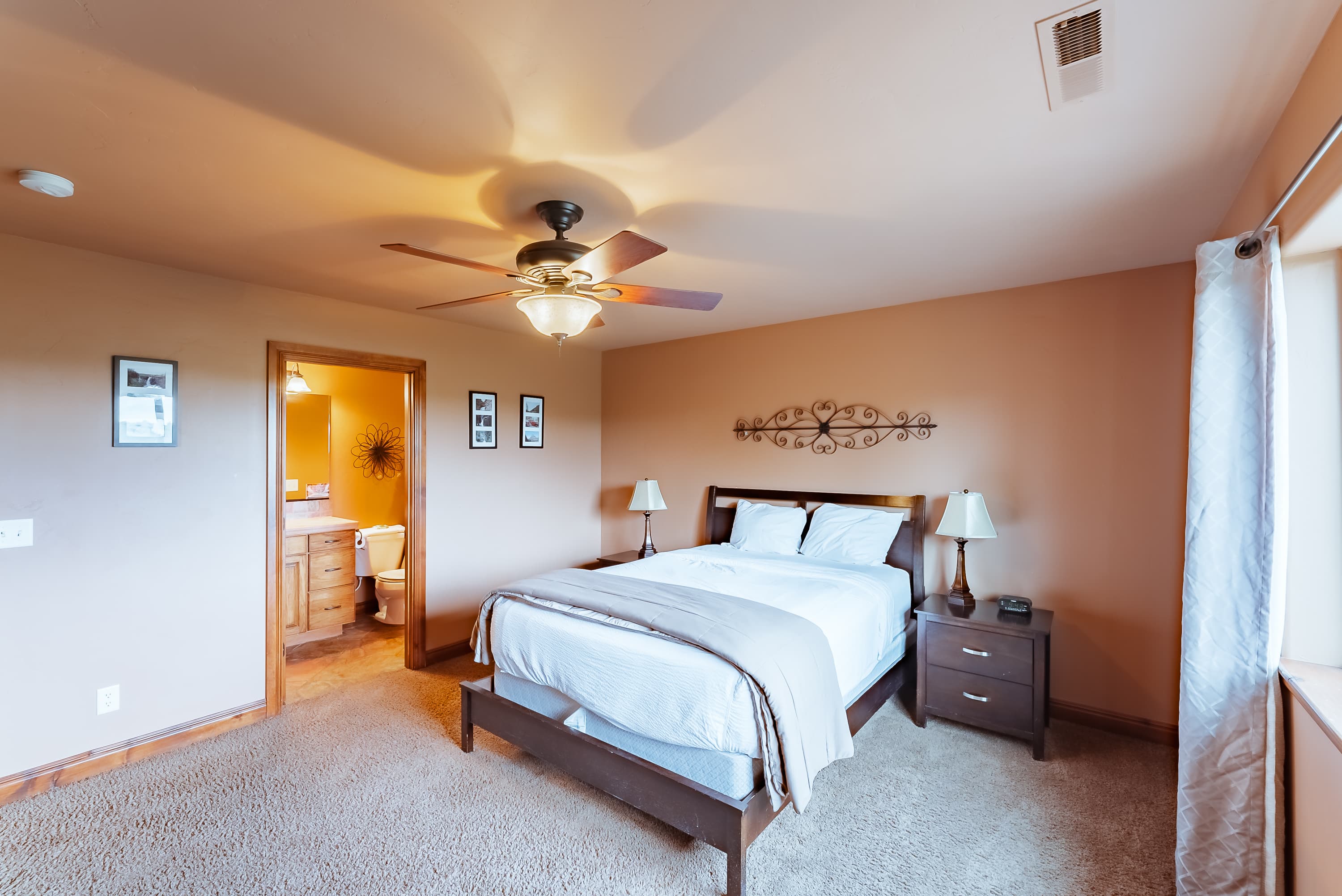 Cozy bedroom with a ceiling fan, bedside lamps, and an adjoining bathroom.