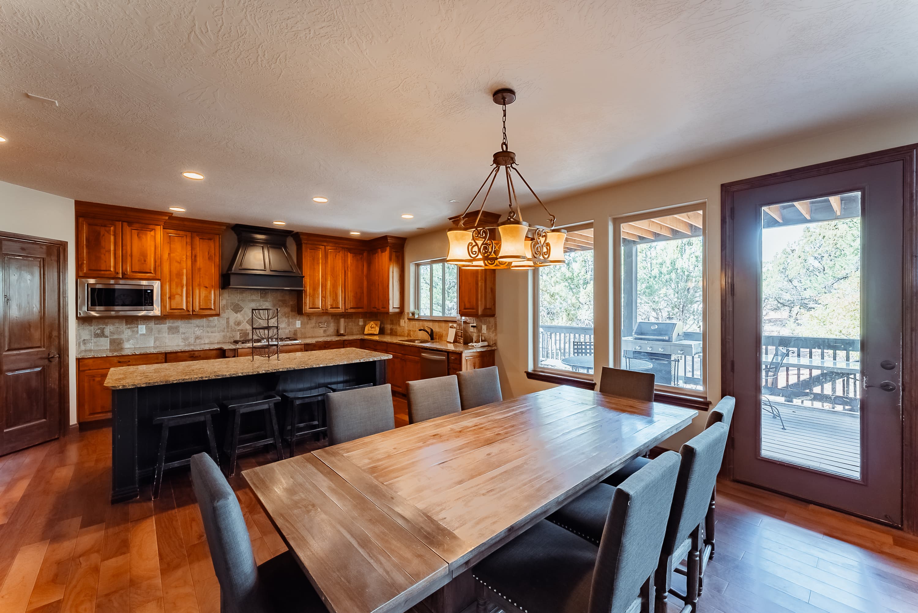 A modern kitchen with wooden cabinets, a large dining table, and bright windows leading to a deck.