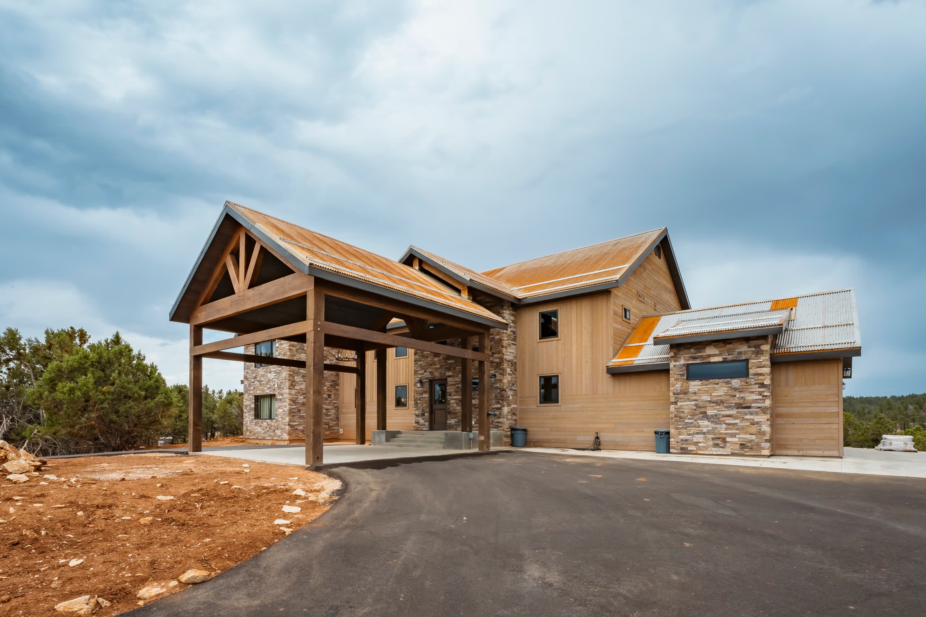 A modern two-story house with a wooden porch and stone accents, set against a cloudy sky.