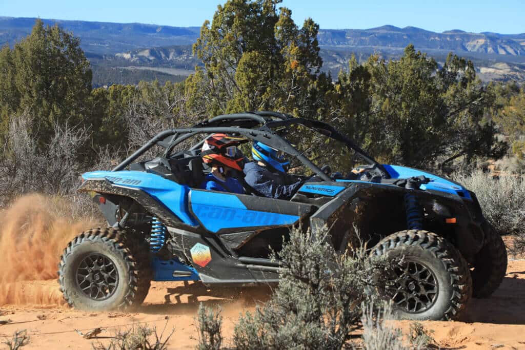 A blue off-road vehicle kicks up dust while driving through a rugged landscape.