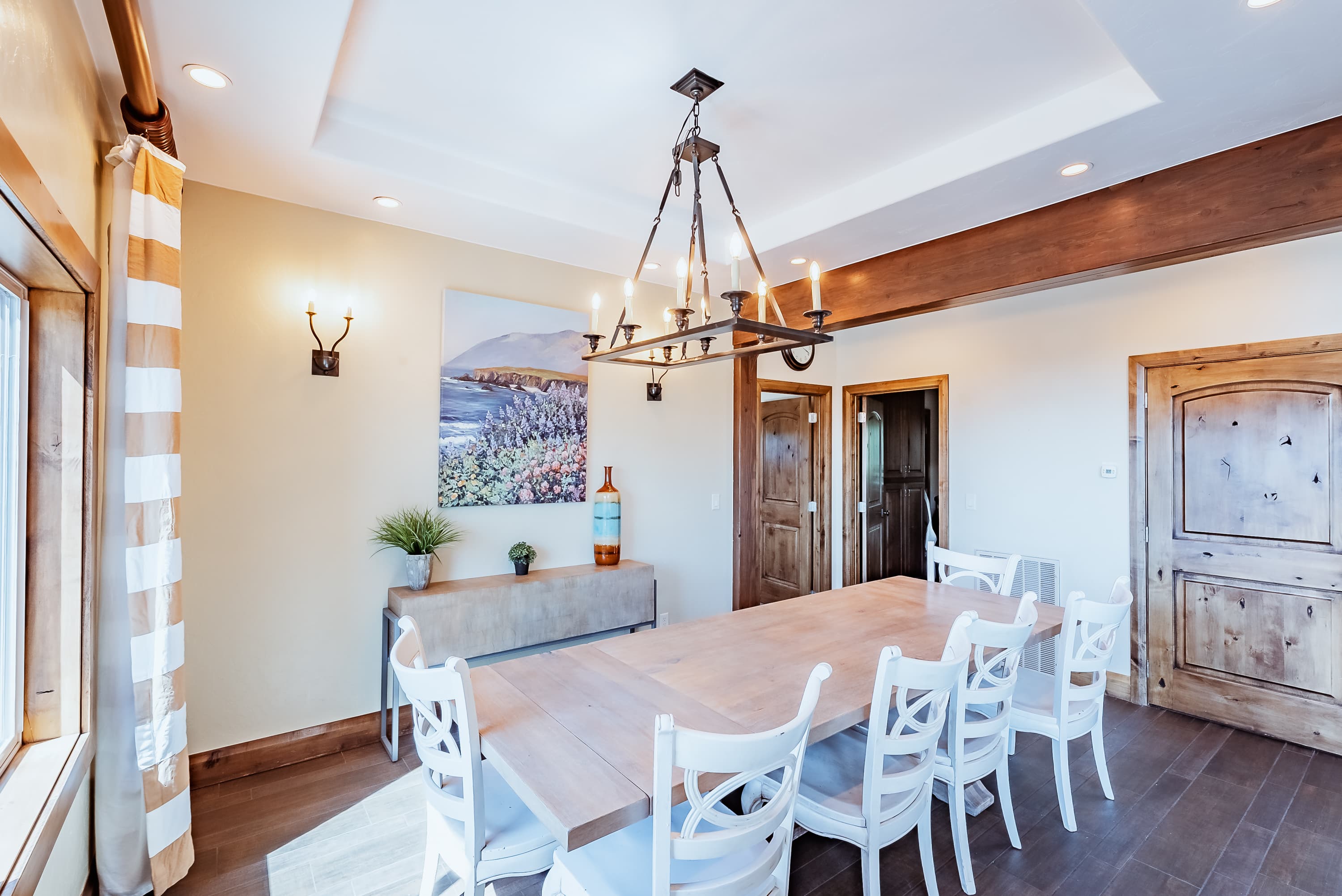 A modern dining room featuring a long wooden table surrounded by white chairs, with warm lighting and artwork on the walls.