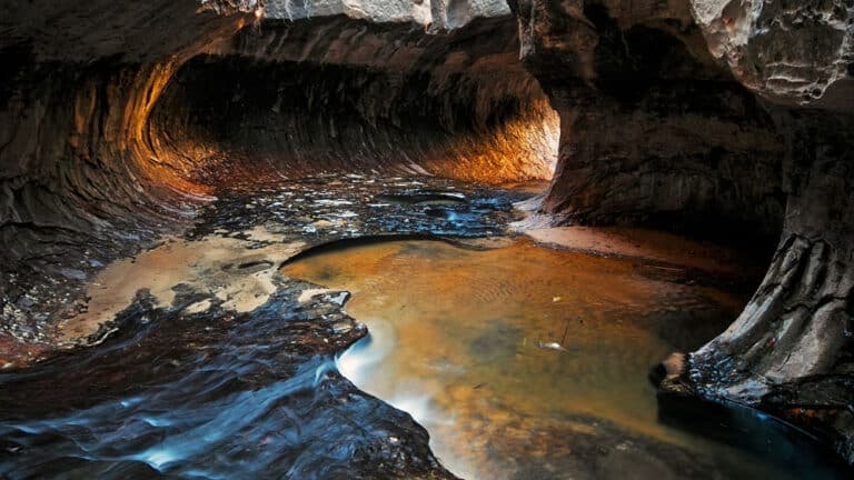 A narrow, water-filled canyon with glowing walls and flowing water.