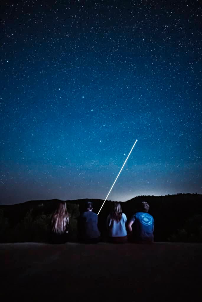 Four people gazing at a starry night sky, with a bright light streaking across.