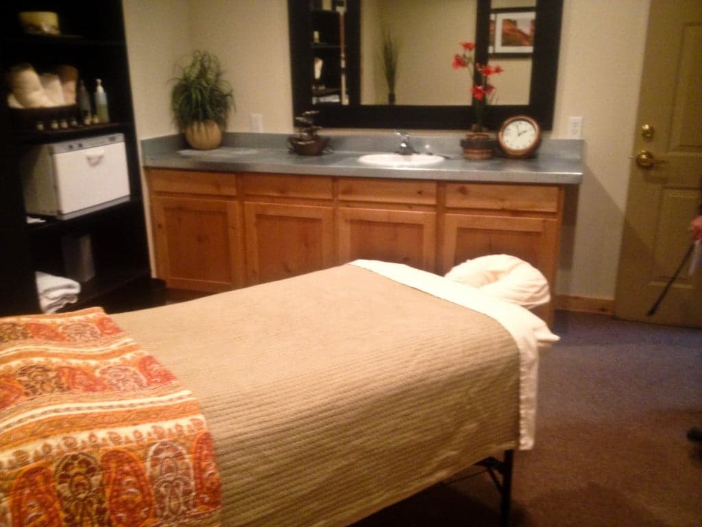 A cozy massage therapy room featuring a massage table, wooden cabinets, and a mirror.