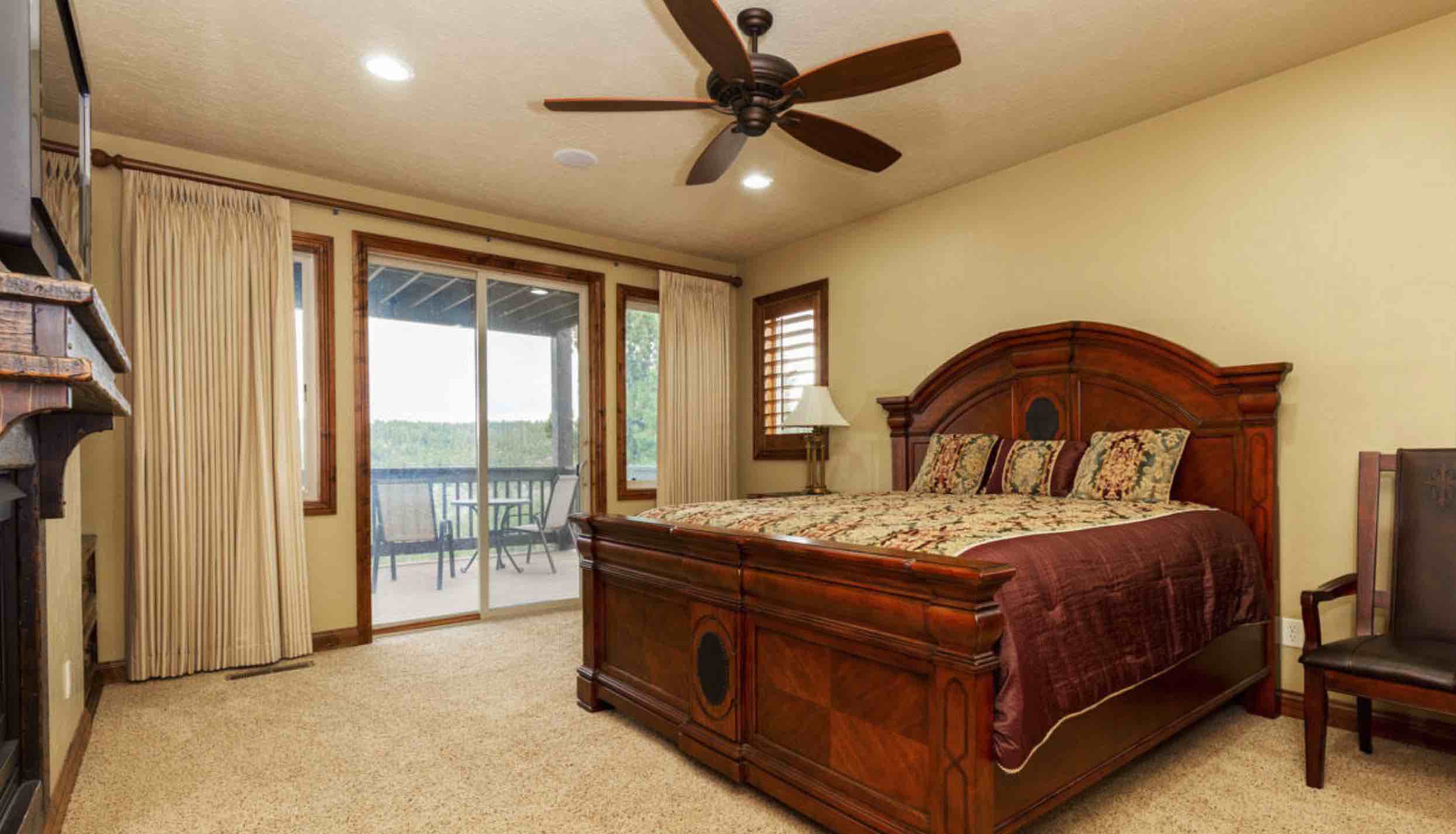A cozy bedroom featuring a wooden bed, large windows with sliding doors, and a ceiling fan.