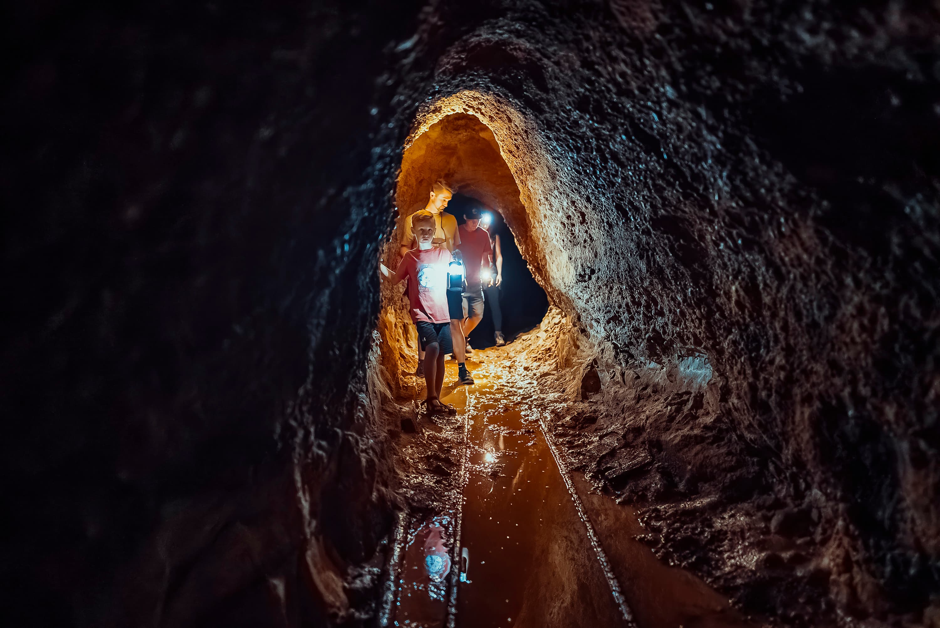 Two people walking through a dimly lit cave with flashlights.