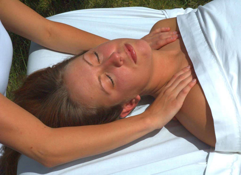 A woman receiving a massage while lying on a white sheet outdoors.