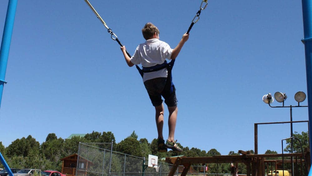 A child swings high on a swing set against a clear blue sky.