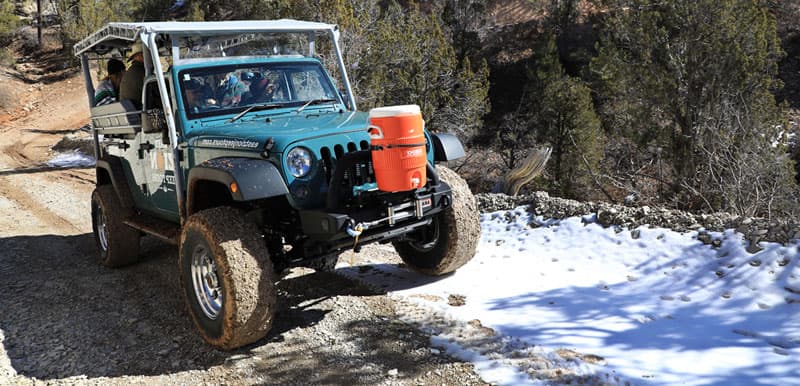 A rugged green Jeep parked on a dirt trail near a patch of snow.