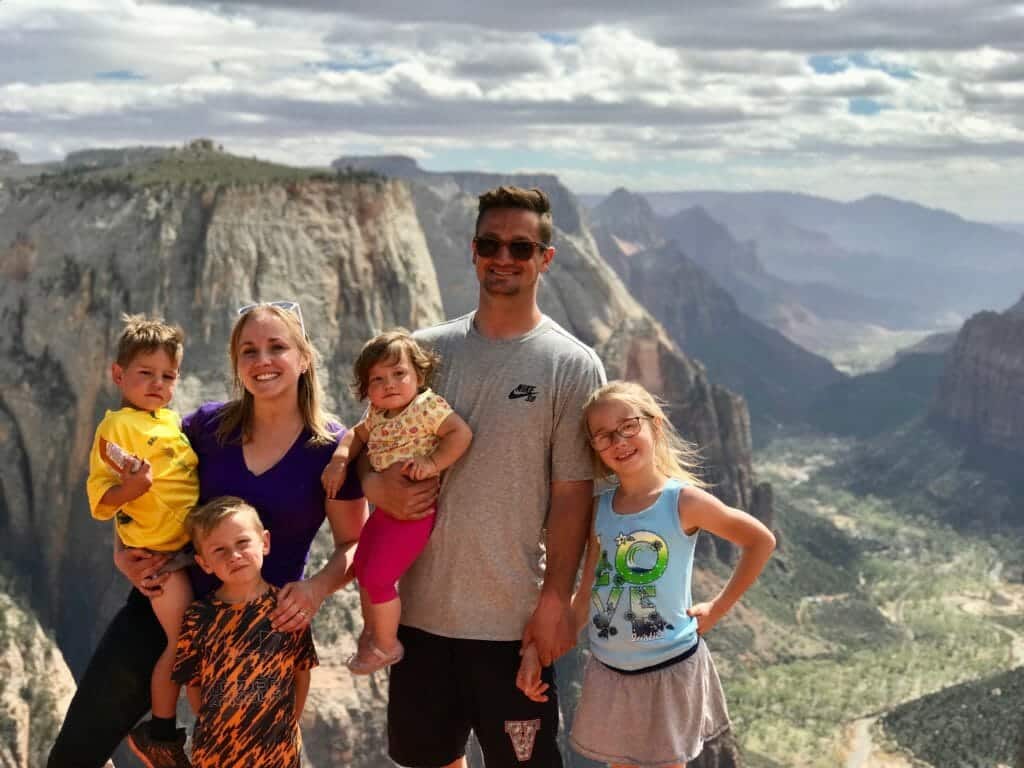 A family of five smiles together at the edge of a scenic canyon.
