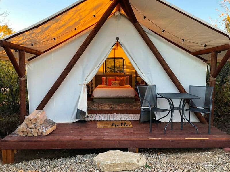 A cozy glamping tent with a wooden deck, featuring a bed and seating area.