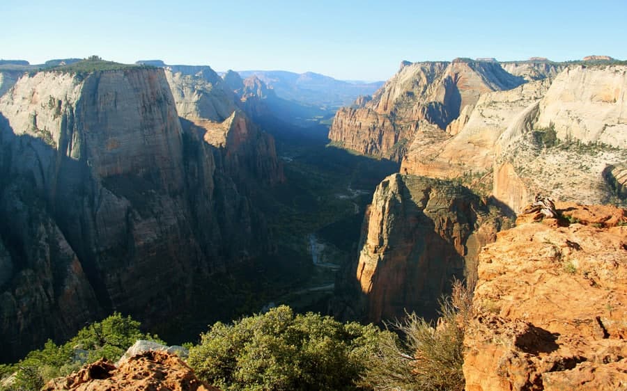 A panoramic view of a vast canyon landscape with steep rock formations under a clear blue sky.