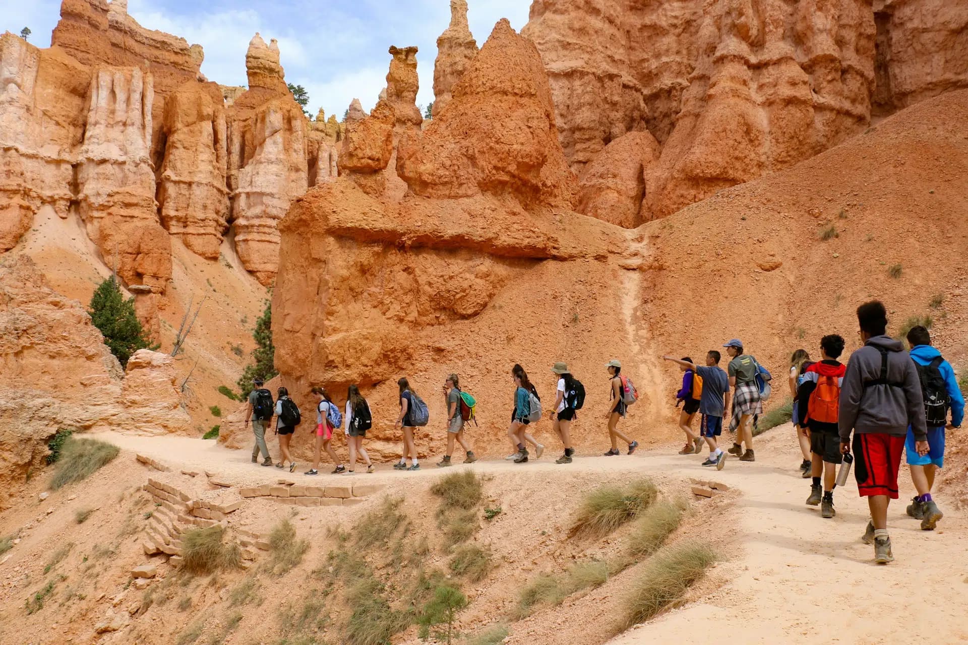 A group of hikers walks along a winding trail in a rocky, orange-hued landscape.