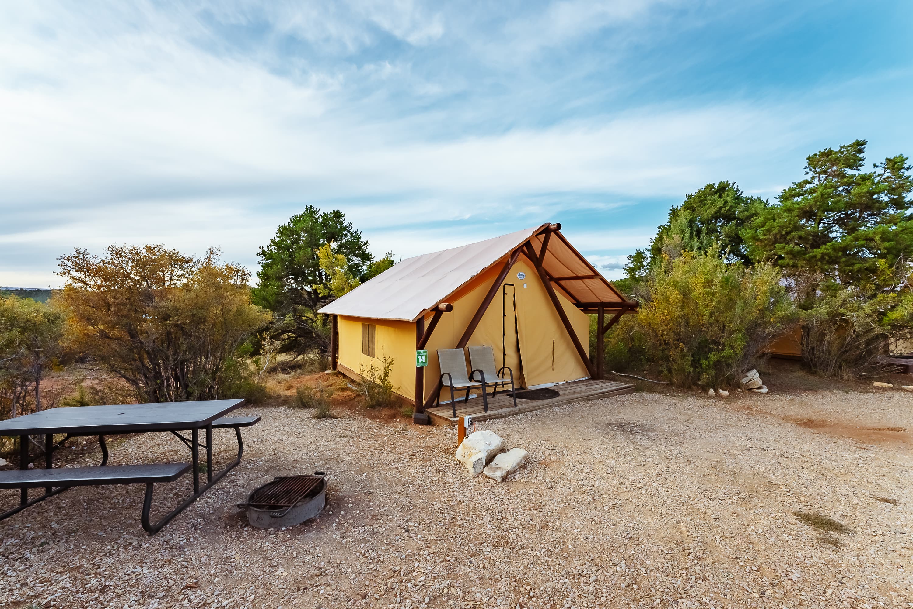 A cozy tent cabin surrounded by shrubs and a picnic area.