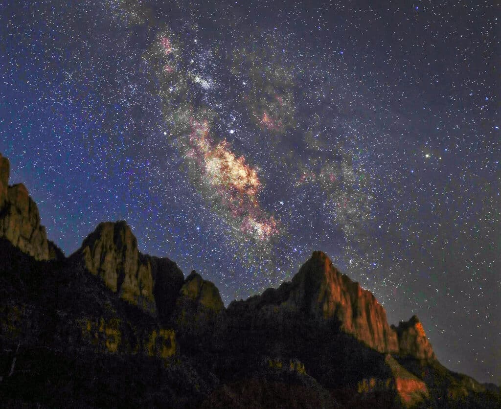 A bright Milky Way galaxy spans a starlit sky above rugged mountain silhouettes.