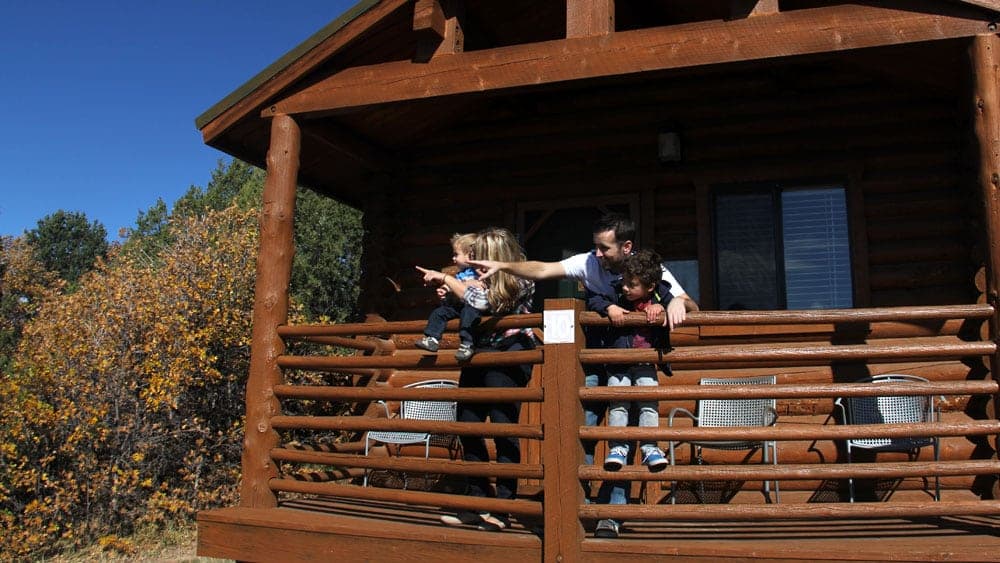 A family stands on a cabin porch, looking out and pointing at the scenery.