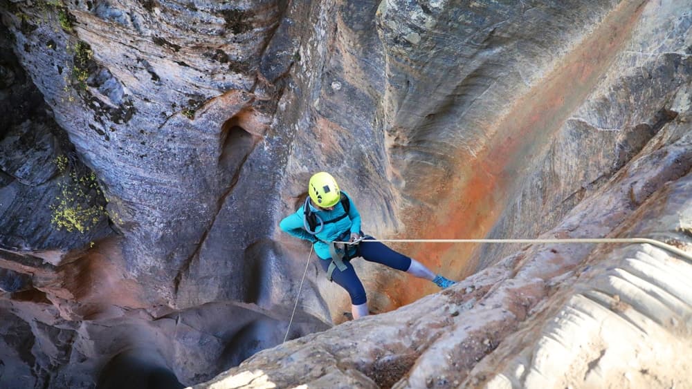 A climber rappels down a rocky canyon while wearing a helmet and harness.