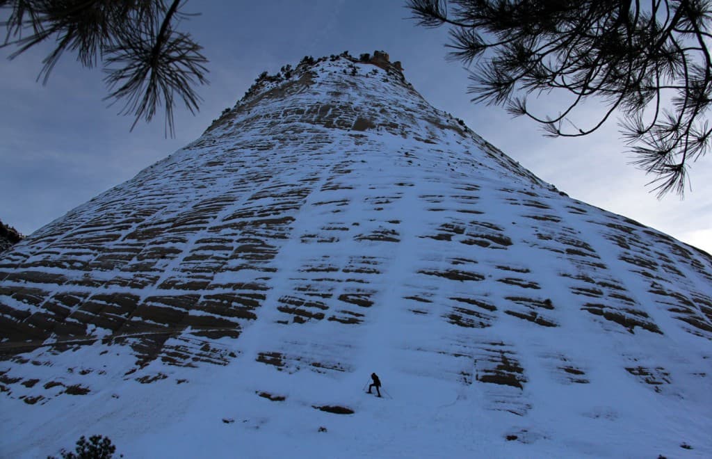 A climber ascends a steep, snow-covered rock face under a cloudy sky.