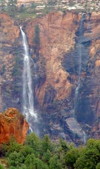 Waterfalls cascading down a rocky cliffside surrounded by greenery.