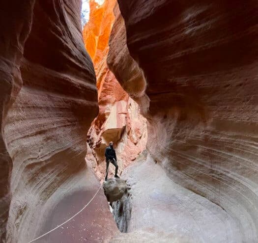 A person stands on a rock in a narrow, colorful canyon.