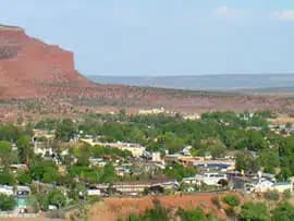 A panoramic view of a small town surrounded by green trees and red rock formations.