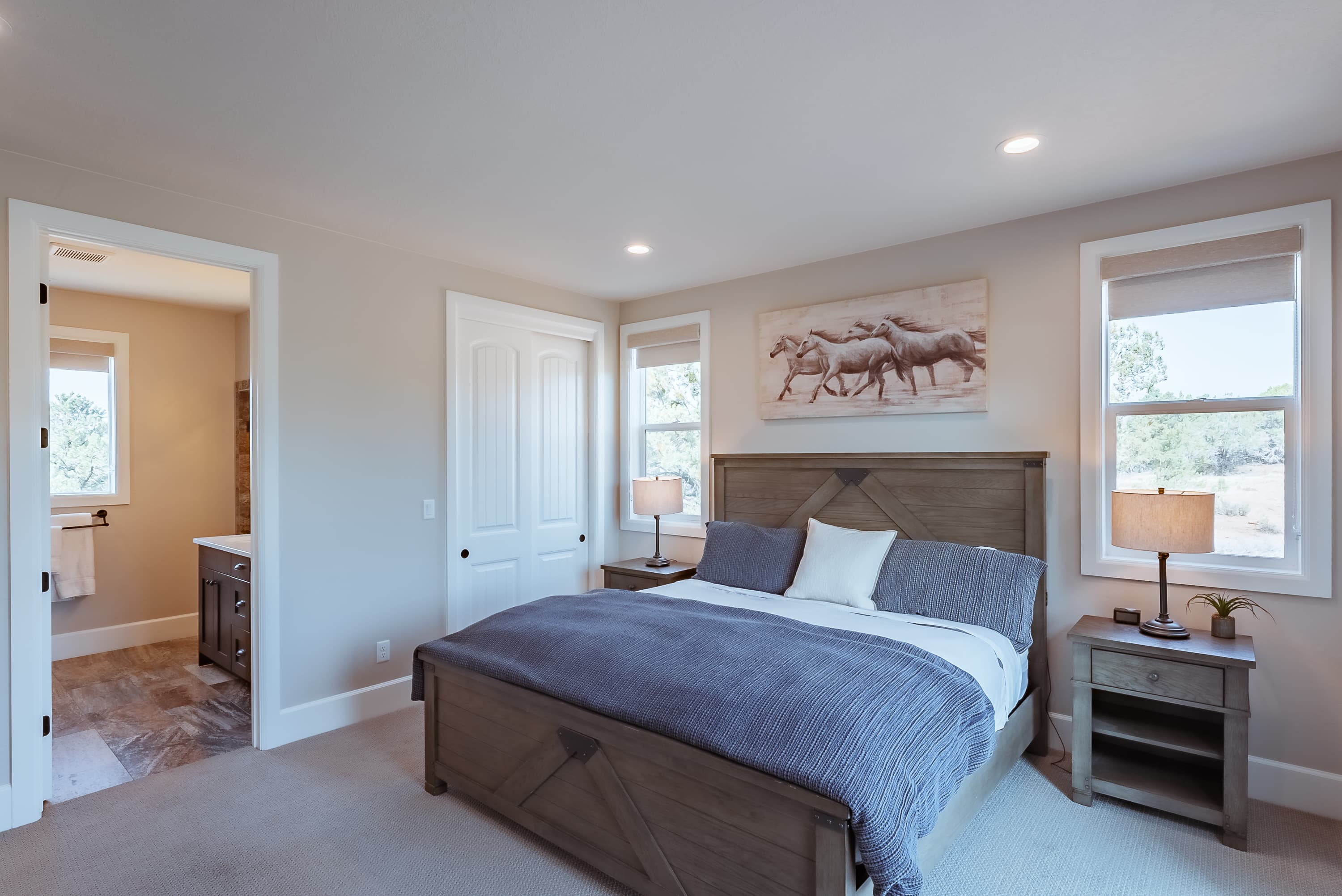 A cozy bedroom featuring a large bed, two bedside tables with lamps, and a painting of horses on the wall.