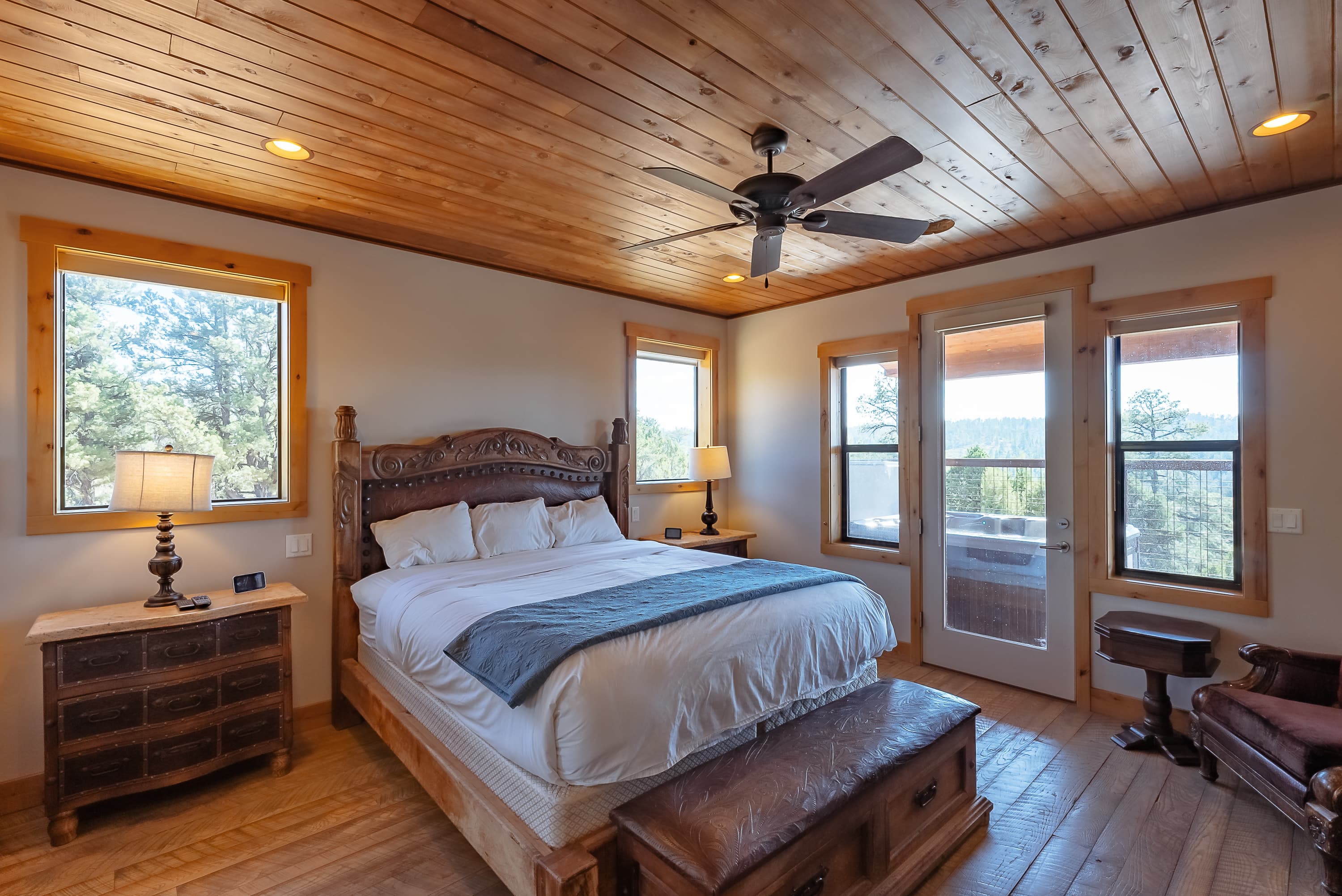 Cozy bedroom featuring a wooden bed, two lamps, and large windows with outdoor views.