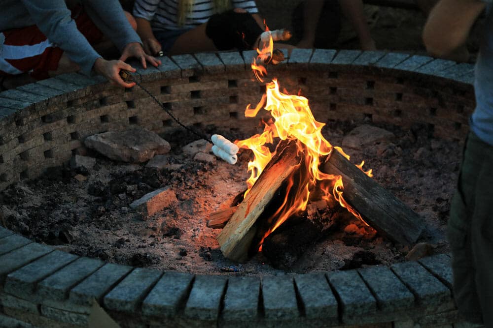 A person roasting a marshmallow over a fire in a stone fire pit.