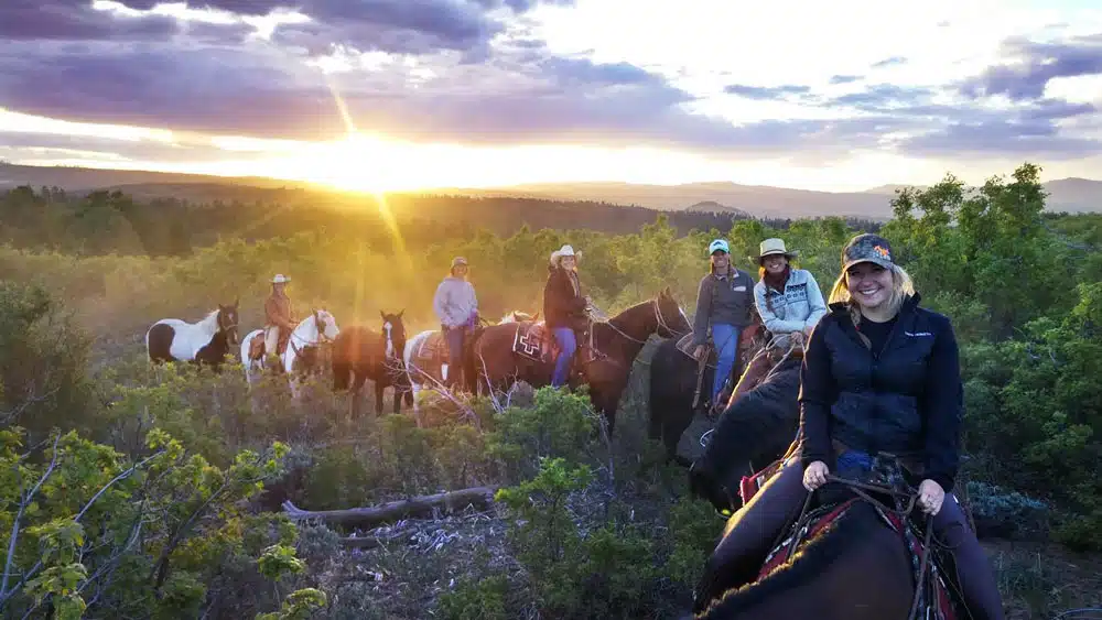 A group of horseback riders enjoy a sunset in a natural landscape.