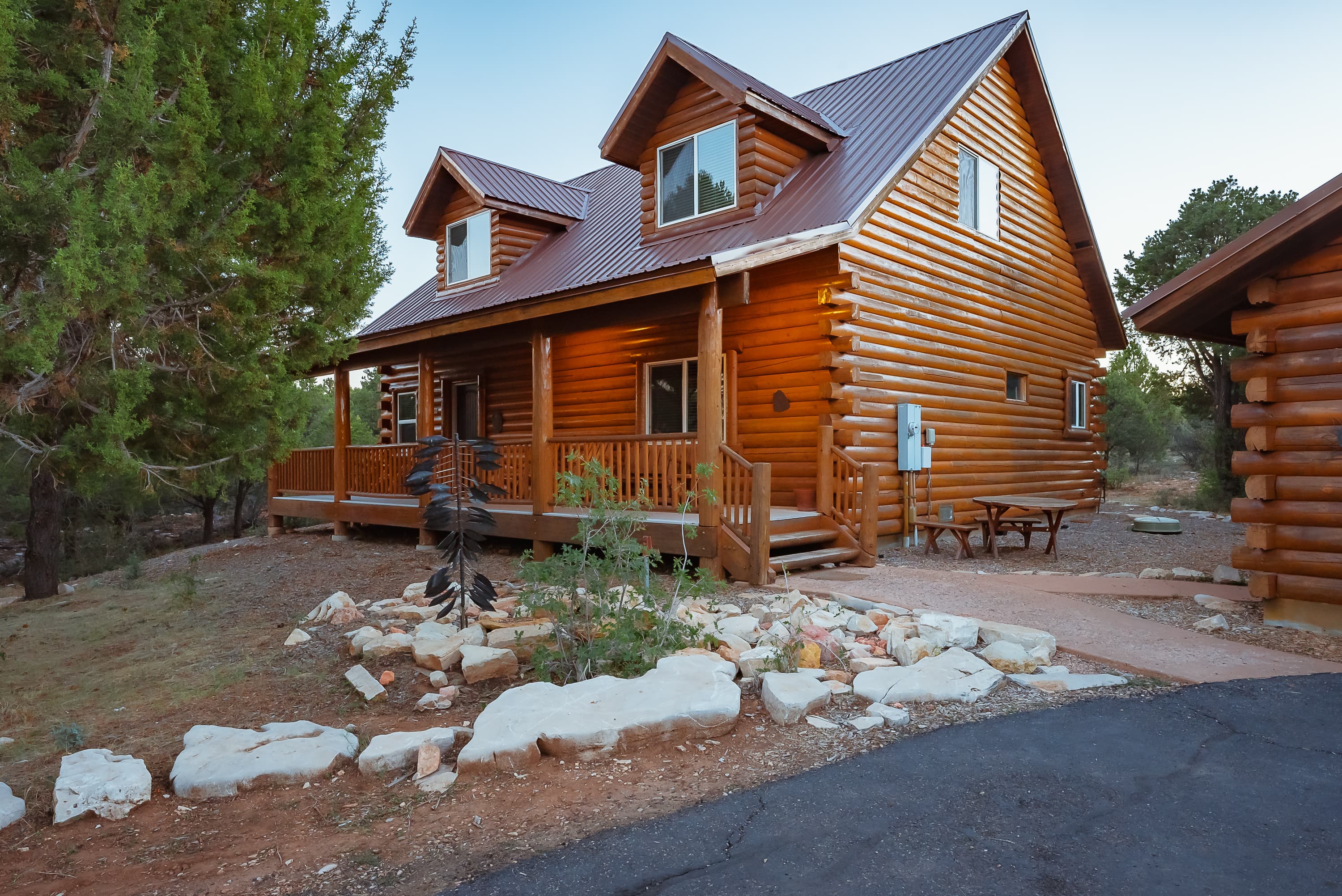 A two-story log cabin surrounded by trees and landscaping.