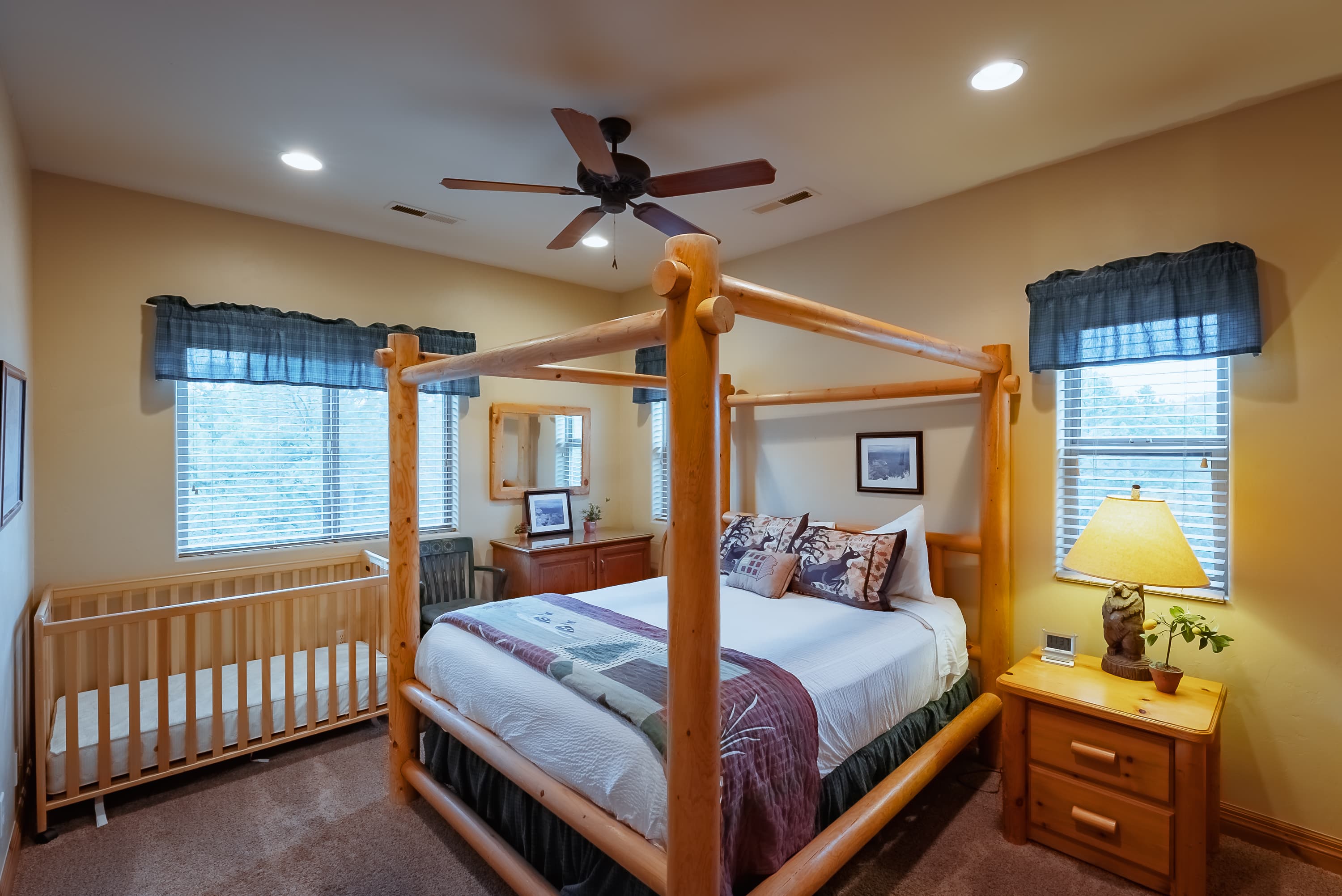 A cozy bedroom featuring a wooden four-poster bed, a crib, and warm lighting.