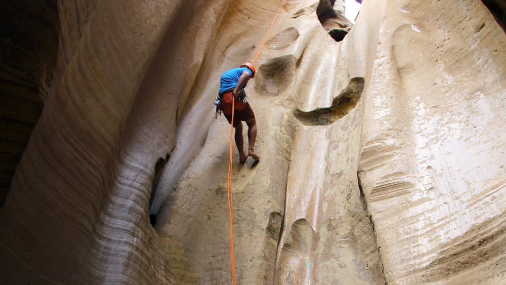 A climber rappels down a textured rock canyon.