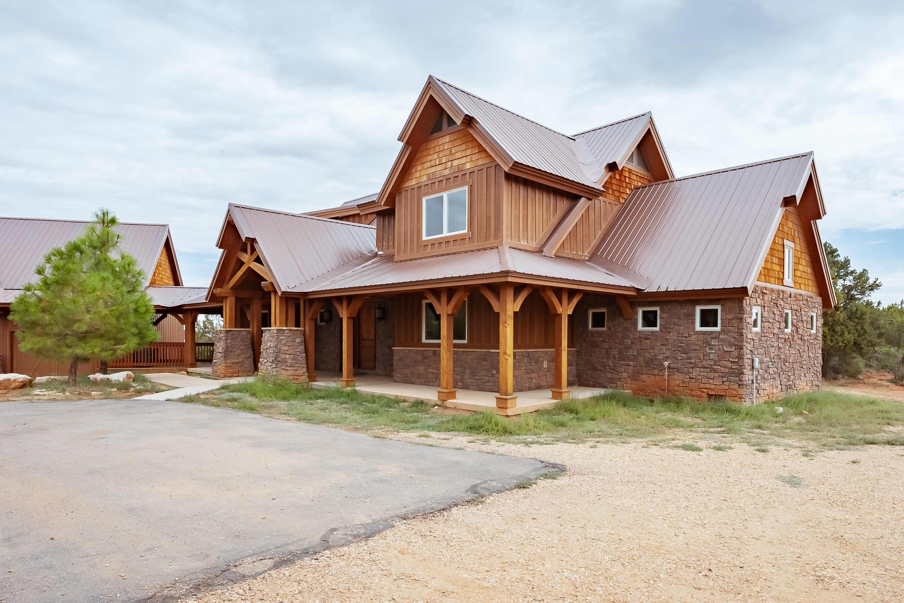 A large, rustic-style house with a combination of wood and stone exterior under a cloudy sky.