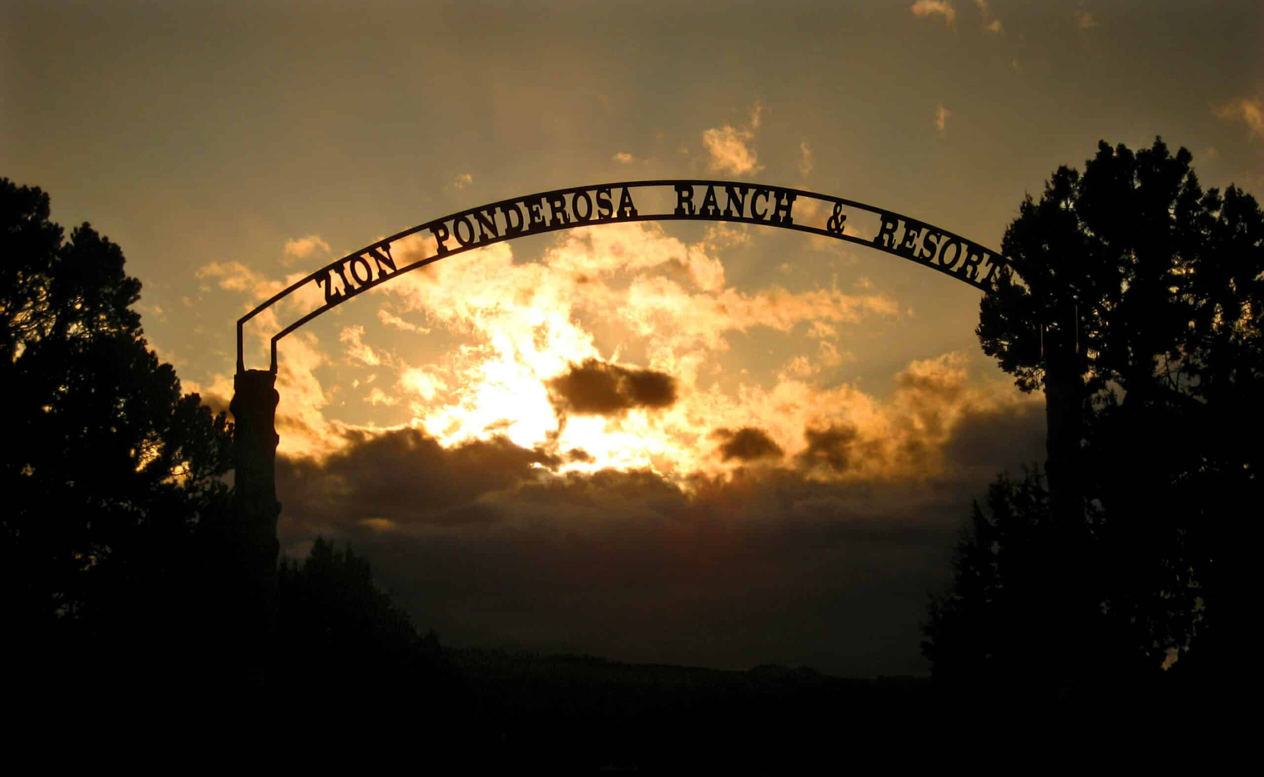 Silhouette of the Zion Ponderosa Ranch & Resort entrance sign against a sunset.