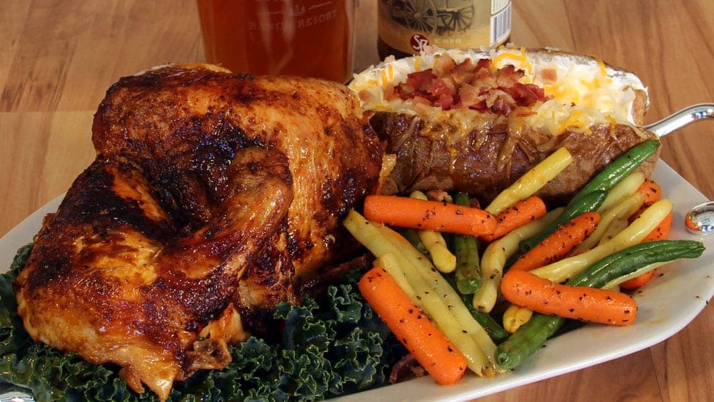 A plate of roasted chicken, a loaded baked potato, and a colorful mix of steamed vegetables.