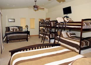 A spacious bedroom featuring a queen bed, multiple bunk beds, and a wall-mounted television.
