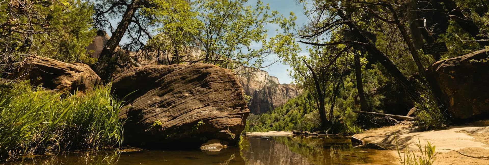 A serene river meanders through a lush landscape with large rocks and trees under a clear sky.