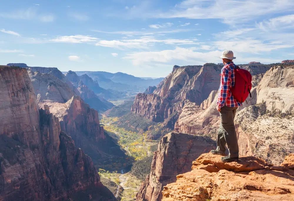 A hiker stands on a rocky ledge overlooking a vast canyon landscape.
