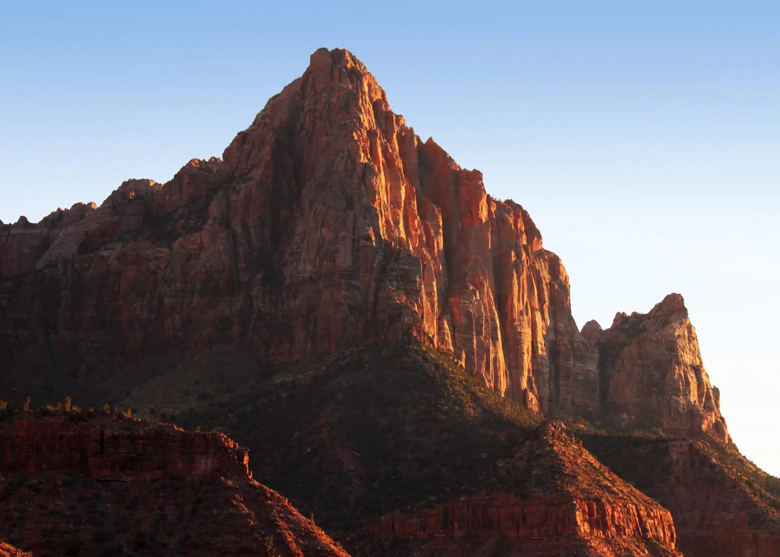 A towering red rock formation against a clear blue sky.