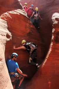 a tour guide safely leads tourists down a red rock slot canyon while canyoneering