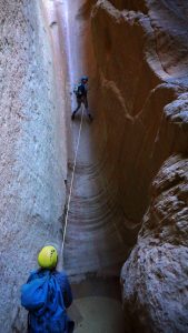 a canyoneering guide holds the rope for a tourist to safely repel down a slot canyon near zion national park