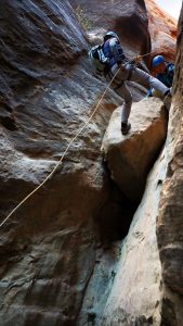 a woman repels down a rock near zion national park while a guide stands by to help