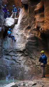 a group of men watch as an adventurer repels down a rock wall near zion national park