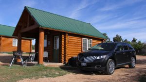 a black Lincoln SUV parked outside of a cowboy cabin, featuring a fire grill, at Zion Ponderosa Ranch