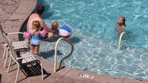 a father and his 3 daughters are swimming in a pool on a hot day near Zion National Park