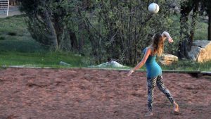 A woman in activewear gets ready to serve a volleyball on a beach volleyball court at Zion Ponderosa Ranch