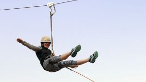 a woman wearing a helmet holds her arms out while riding on a zipline near Zion National Park