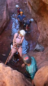 a group of tourists repels down a rock wall with a canyoneering guide