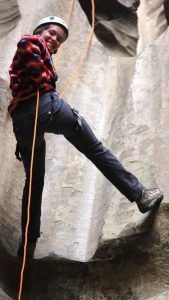a girl smiles down at camera while repelling down a rock wall near zion national park