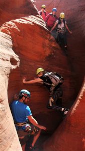 a group of tourists carefully scrambles down a rock wall while canyoneering near Zion national park in Utah
